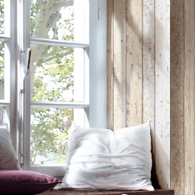 Assento de janela em madeira com almofadas branca e roxa junto a janela aberta