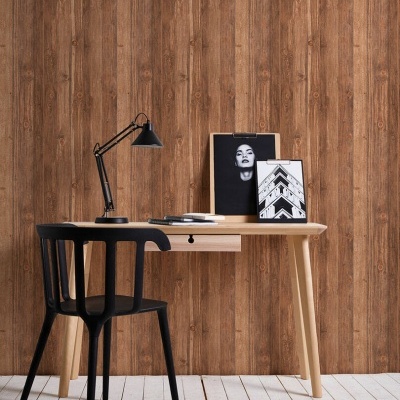 Secretária de madeira clara com cadeira preta, candeeiro e molduras em ambiente com parede de padrão madeira.
