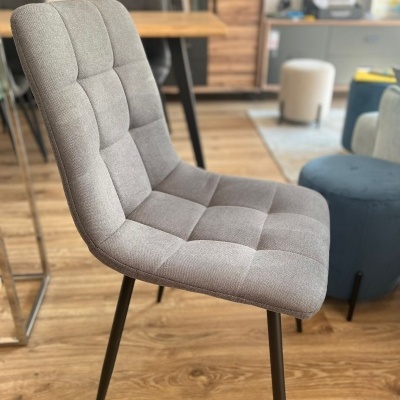 Cadeira estofada cinza com pernas pretas num ambiente interior moderno