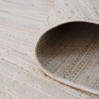 Tapete bege claro com textura em relevo e verso tecido rústico, parcialmente enrolado sobre superfície clara