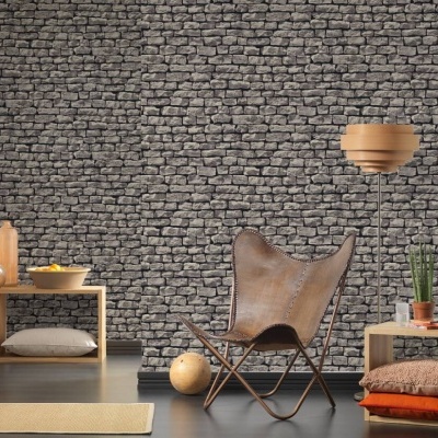 Sala com parede em pedra, cadeira de pele castanha, prateleira e luminária de madeira, mesa pequena com almofadas e planta