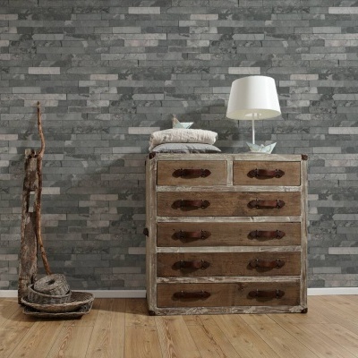 Móvel de madeira rústica com cinco gavetas e candeeiro branco junto a escultura de madeira numa parede de azulejos cinzentos.