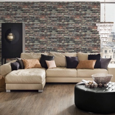 Sofá chaise longue bege com almofadas coloridas contra parede de tijolos rústicos, puff preto e chão de madeira