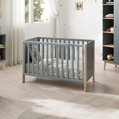 Berço de bebé cinzento com pés de madeira clara num quarto neutro com almofada e roupa de cama com estrelas