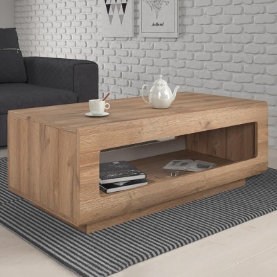 Mesa de centro em madeira natural com livros, revista, bule e chávena, tapete cinza às riscas, sofá preto, parede de tijolo branco.