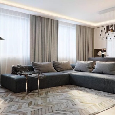 Sala de estar moderna com sofá cinzento, candeeiro de pé, planta, e cozinha ao fundo.