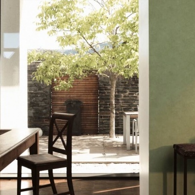 Sala de jantar com mesa e cadeiras de madeira, parede verde, porta aberta para pátio exterior com árvore e muro de pedra