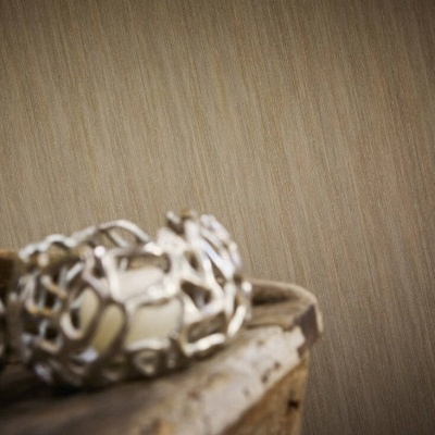 Pulseira metálica prateada com padrão curvilíneo sobre madeira envelhecida