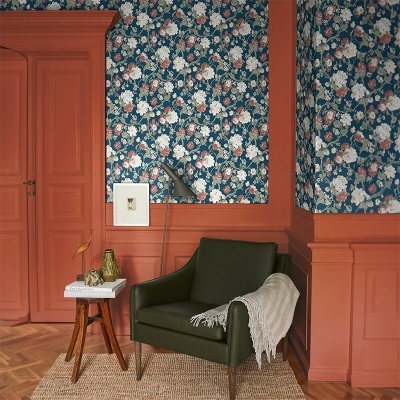 Poltrona verde escuro com manta sobre tapete bege, parede florida azul e porta cor terra.