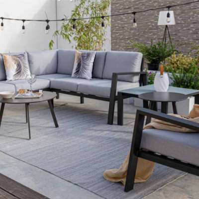 Conjunto de sofá de canto e poltrona cinza com mesas pretas em jardim exterior