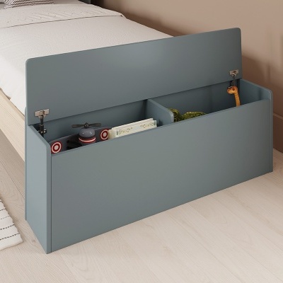 Cama individual com móvel baú azul aberto ao lado, em quarto com parede bege e chão de madeira clara.