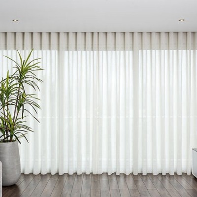 Cortinas brancas translúcidas em janela com planta e móvel baixo ao lado