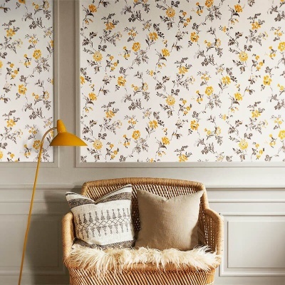 Poltrona de vime com almofadas e manta, candeeiro amarelo e janelas com cortinas florais