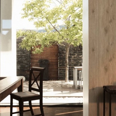 sala de jantar com mesa e cadeira de madeira junto a janela aberta para jardim com árvore