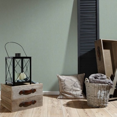 Conjunto decorativo com lanterna preta, caixa de madeira clara, almofada, cesta de vime, manta cinza, moldura em forma de A e painel preto em fundo verde claro