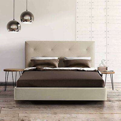 Cama de casal com cabeceira estofada bege e roupa de cama castanha, mesas de cabeceira redondas em madeira, lâmpadas pendentes metálicas.