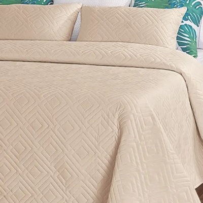 Colcha bege com padrão geométrico e almofadas decorativas em cama