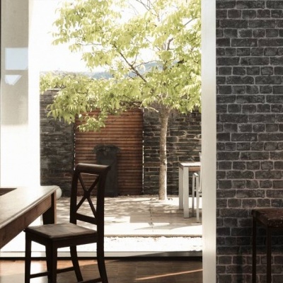 Sala de jantar com parede de tijolos cinza e mesa de madeira escura junto a grande janela para pátio exterior