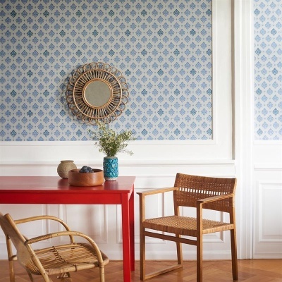Mesa vermelha com cadeiras em vime em sala com papel de parede azul e espelho redondo de vime na parede