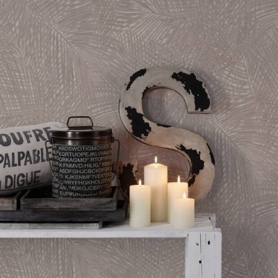 Velas brancas, jarra preta com texto francês, rolo de papel com texto e letra decorativa 'S' sobre bancada branca