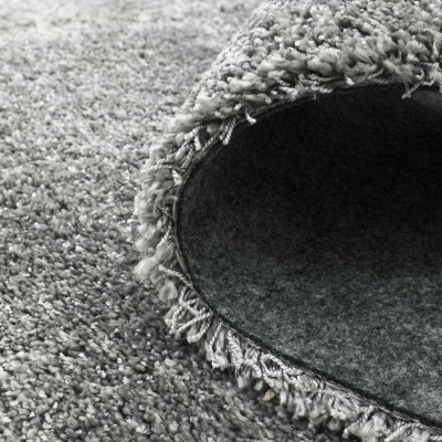 Tapete cinzento felpudo com pelo comprido e base em feltro escuro.
