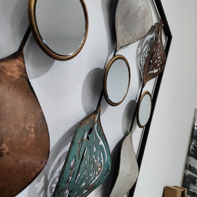 Espelho decorativo com múltiplos pequenos espelhos redondos em moldura preta e formas metálicas coloridas
