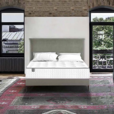 Quarto com cama de colchão branco e cabeceira cinza, janelas arqueadas e tapete vermelho e cinza no chão