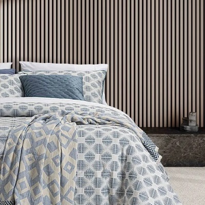 Cama com roupa de cama padrão geométrico azul e branco e manta bege e azul junto a cabeceira de madeira e bancada em mármore escuro