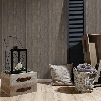 Ambiente com chão em madeira clara, papel de parede riscado castanho, caixas de madeira, lanterna preta, almofada, cesto de vime e escadote