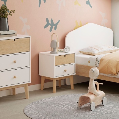 Quarto infantil com mobília branca e madeira clara, parede rosa com folhas, tapete cinza e brinquedo de coelho