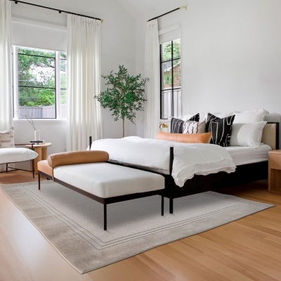 Quarto com cama e banco com almofadas decorativas, cortinas brancas e planta verde