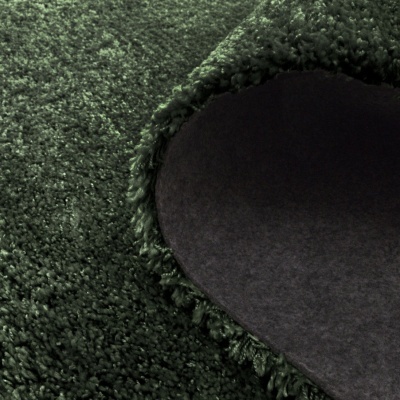 Tapete verde felpudo com a parte inferior cinzenta visível e franja na dobra