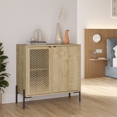 Móvel moderno em madeira clara com padrão rattan, ao lado de planta, num quarto com cama e cabeceira estofada.