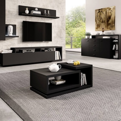 Sala de estar com móveis pretos, televisão e mesa de centro em tom escuro sobre tapete cinzento.