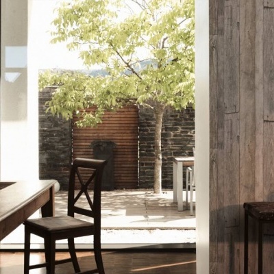 Sala de jantar com mesa e cadeira de madeira junto a porta aberta para pátio com árvore