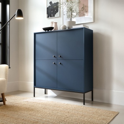 Armário azul escuro com quatro portas e puxadores metálicos numa sala decorada com plantas e candeeiro.