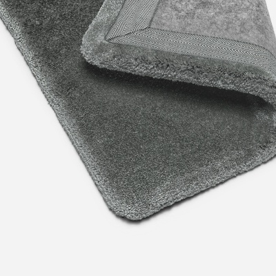 Tapete cinza felpudo com borda costurada em superfície branca