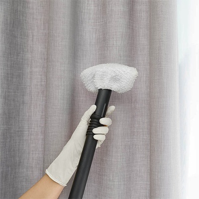 Mão com luva segurando cabo preto com cabeça de limpeza branca em frente a cortina cinza