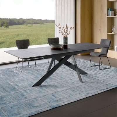 Mesa de jantar cinzenta escura com cadeiras cinzentas e tapete azul numa sala iluminada