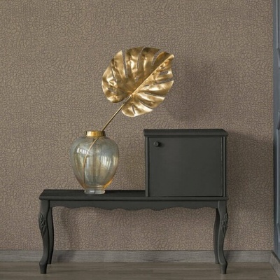 Mesa preta com vaso de vidro dourado e folha dourada decorativa, ao lado de pequeno armário preto, parede castanha clara texturada ao fundo.