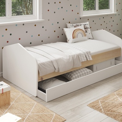 Cama individual branca com gaveta e roupa de cama branca num quarto infantil luminoso