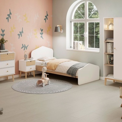 Quarto infantil com mobília branca e madeira clara, paredes rosa e cinza, cama com colcha bege e cinza.