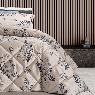 Edredão e almofada bege com padrão floral cinza e azul escuro numa cama contra parede de ripas castanhas.