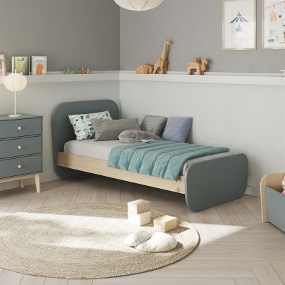 Cama infantil de madeira com colcha azul e almofadas, cómoda azul, tapete bege redondo em quarto cinzento