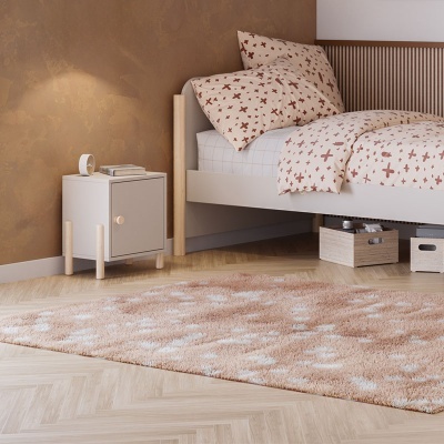 Quarto com cama de madeira clara, roupa de cama bege com cruzes castanhas e tapete felpudo bege claro