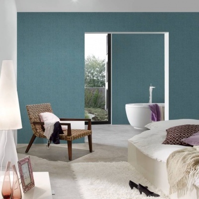 Quarto moderno com cadeira de vime, cama branca, almofadas roxas, manta bege e candeeiro de pé branco