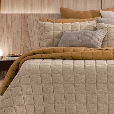 Cama com roupa de cama bege e castanha em ambiente com parede de madeira e prateleira com livros