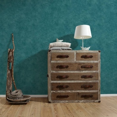 Cómoda de madeira rústica com cinco gavetas, almofadas e lâmpada sobre, parede azul texturizada ao fundo