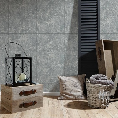 Ambiente decorativo com candeeiro, caixa de madeira, almofada e cesto com manta sobre chão de madeira e parede texturizada cinzenta.