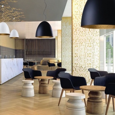 Salão moderno com cadeiras pretas, mesas de madeira e luminárias pendentes